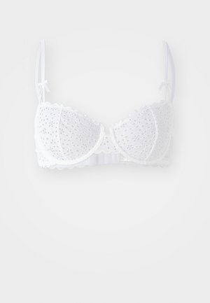 Soutien-gorge en dentelle blanche avec des bords festonnés, des bonnets rembourrés et des motifs floraux décoratifs. Il dispose de bretelles réglables et d'une fermeture à crochets au dos.