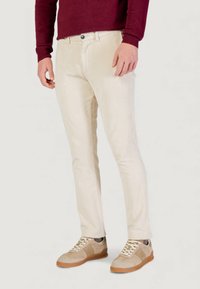 Pantalones beige de pana con un corte ajustado, que presentan sutiles costillas verticales. Combinados con zapatillas de gamuza color marrón claro y un suéter granate.