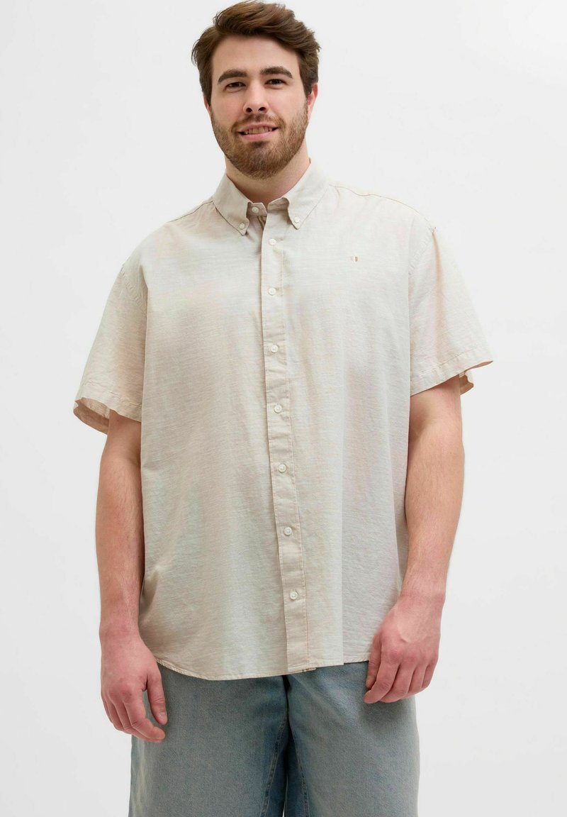 Chemise à manches courtes en tissu beige clair, présentant un col, des boutons sur le devant et un petit logo sur la poitrine.