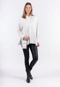 Biała koszula z guzikami o luźnym kroju, w zestawieniu z czarnymi skórzanymi legginsami i botkami za kostkę. Zawiera małą białą torebkę na ramię.
