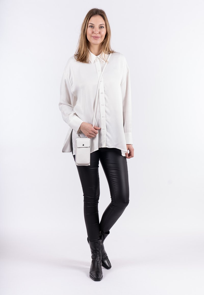 Biała koszula z guzikami o luźnym kroju, w zestawieniu z czarnymi skórzanymi legginsami i botkami za kostkę. Zawiera małą białą torebkę na ramię.