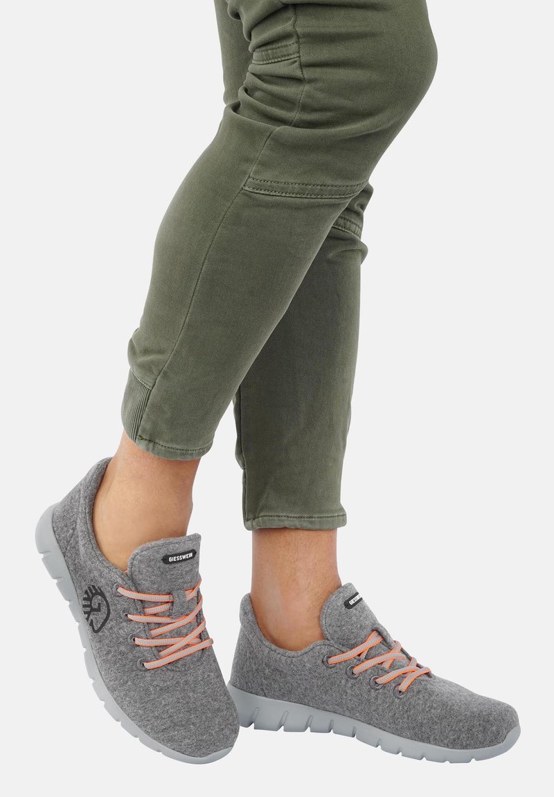 Graue Filzschuhe mit einer runden Spitze, orangefarbenen Schnürsenkeln und einem Logo an der Seite; kombiniert mit olivgrünen Cropped-Hosen. Gummisohle sichtbar.
