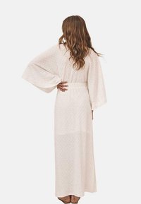 Vestido largo de estilo kimono en un suave color rosa claro con mangas anchas, que presenta un patrón texturizado y un lazo en la cintura, llegando hasta los tobillos.