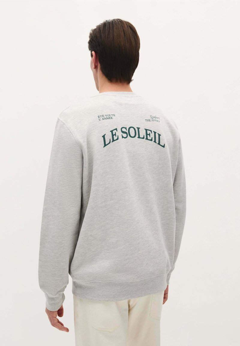 Sweatshirt gris à manches longues, avec le texte imprimé "LE SOLEIL" au dos en vert, texture douce, et poignets et ourlet côtelés.