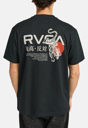 Polo de algodón negro con un gran gráfico de un tigre blanco, un sol rojo y texto en la parte posterior. Manga corta y diseño de ajuste relajado.
