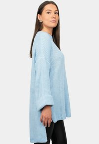 Maglione lavorato a maglia blu chiaro con una vestibilità ampia, caratterizzato da tessuto testurizzato, maniche lunghe e polsini arrotolati, abbinato a leggings neri.