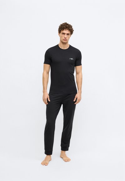 Melna īsroku T-krekls un atbilstošas bikses ar piegulošu dizainu, gludu tekstūru un smalku logotipu uz krūšu kabatas.