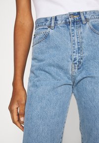 Jeans de cintura alta de tom azul claro, feitos de denim, apresentando um design clássico de cinco bolsos, botão de cobre e costuras visíveis.