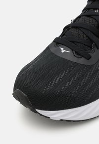Black athletic shoe with a textured mesh upper, white sole, and a sleek design. Features a glossy logo on the vamp and structured lacing.