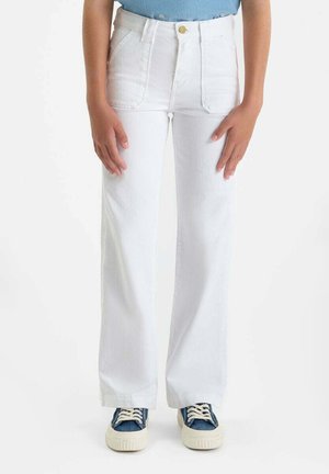 Personne portant un pantalon blanc taille haute à jambes larges avec des poches plaquées à l'avant et des baskets bleues à lacets blancs.