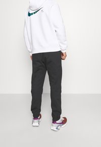 Vit luvtröja med teal Nike-logga på ryggen, matchad med mörkgrå byxor och flerfärgade träningsskor.