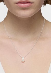 Collar de cadena de plata con un colgante de perla blanca redonda, con un diseño minimalista y textura suave.