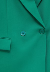 Blazer verde de doble botonadura hecho de tejido texturizado, con dos botones a juego y un solapa entallada con un bolsillo lateral.