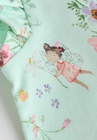 Tissu vert menthe présentant une illustration de fée tenant une fleur, entourée de motifs floraux variés en rose, violet et jaune.