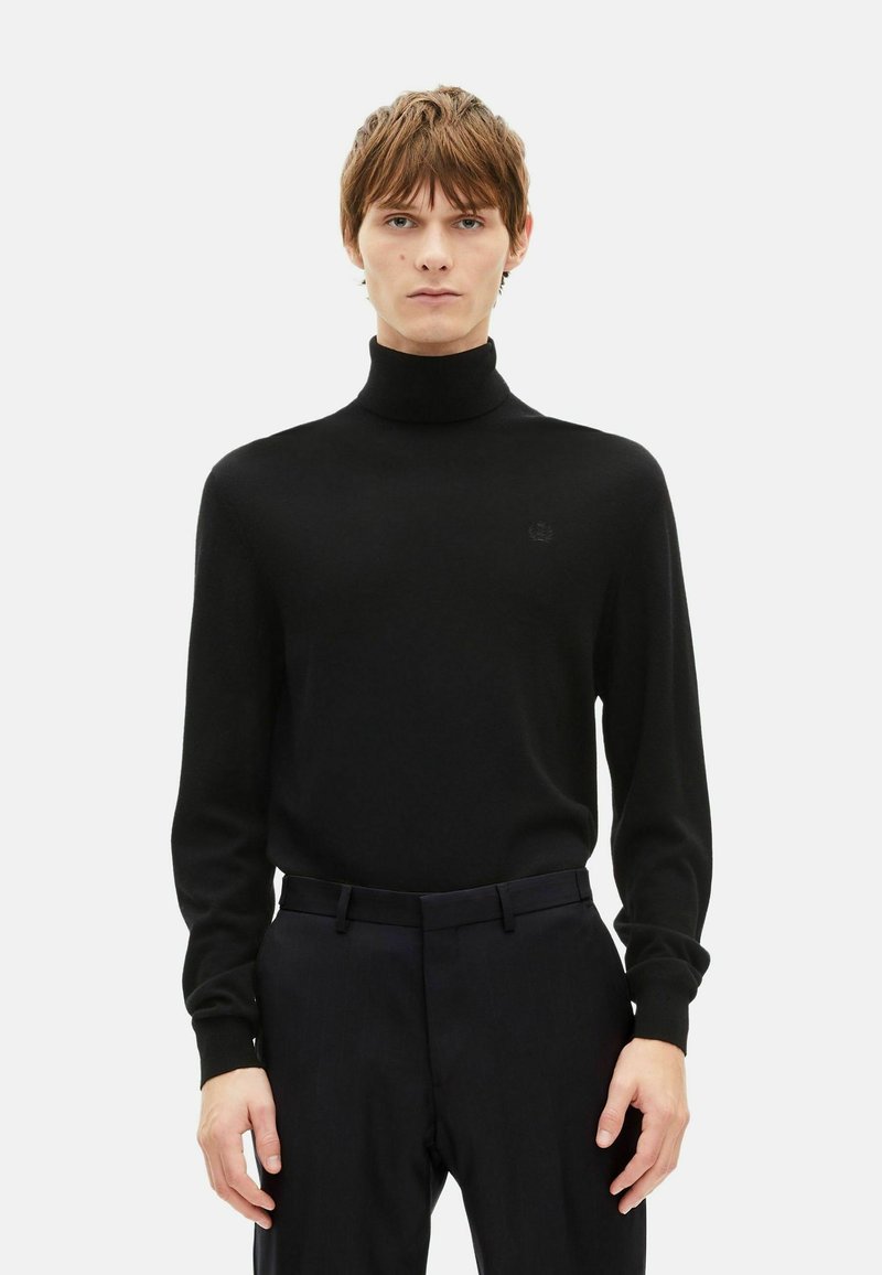 Black turtleneck sweater in soft fabric with long sleeves and a fitted silhouette. Features subtle logo detail at the chest, paired with dark pants.