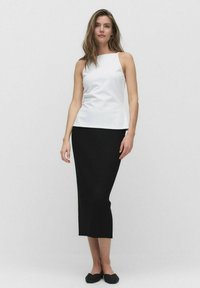 Witte mouwloze top met een hoge halslijn, gecombineerd met een zwarte ribbel midi-skirt. Platte zwarte schoenen maken de look compleet.
