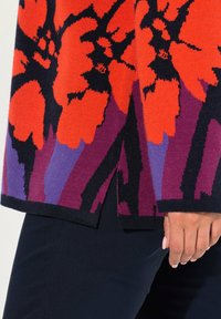 Stickad tröja med stora orange blommönster på svart, med lila och lavendelfärgade detaljer. Har en rak skärning och sidslitsar.