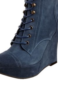 Stivale alla caviglia in suede blu con tacco a zeppa, caratterizzato da allacciatura frontale, punta rotonda e dettagli di cucitura a contrasto. Texture liscia complessivamente.