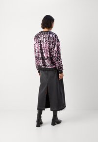 Sudadera de lentejuelas negras y rosas brillantes con un dobladillo negro, combinada con una falda larga de mezclilla oscura con una abertura en la parte trasera, y botas negras de tacón.