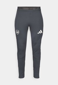 Pantalons de sport gris foncé au design ajusté, avec des rayures blanches Adidas et un logo d'Arsenal sur la cuisse gauche. Texture lisse.