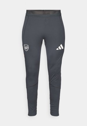Pantaloni sportivi grigio scuro con una vestibilità aderente, dotati di strisce bianche Adidas e di un logo dell'Arsenal sulla coscia sinistra. Tessuto liscio.