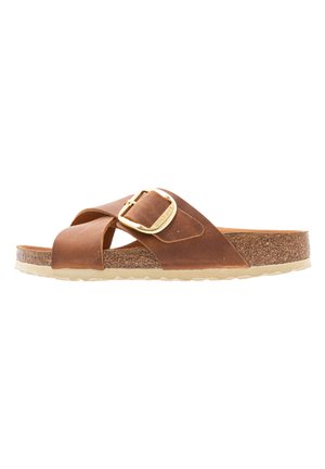 Sandale slide en cuir marron avec une grande boucle dorée, semelle intérieure en liège et semelle extérieure claire texturée, vue de côté.