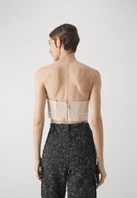Stroppløs beige bodice med teksturert bakside og glidelås lukking, paret med svarte mønstrede vide bukser. Nøytrale farger og strukturert design.