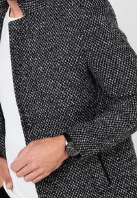Černobílý texturovaný blazer se slim fit střihem, doplněný černými hodinkami se jednoduchým ciferníkem a koženým páskem.