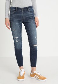 Blåjeans med slitna rivningar, avsmalnande passform och medelhög midja. Matchas med bruna sneakers med vita ränder och en klassisk design.