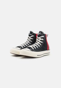 Sneaker alte in tela nera con lacci bianchi e suola in gomma. Accenti rossi sui lati e logo del marchio sulla linguetta. Tessuto testurizzato.