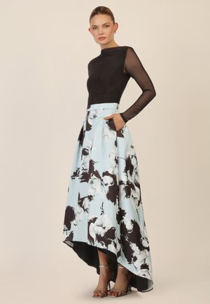 Schwarzes Langarmoberteil kombiniert mit einem fließenden blauen Rock, der mit schwarz-weißen Blumenmustern verziert ist, mit einem High-Low-Saum und seitlichen Taschen.