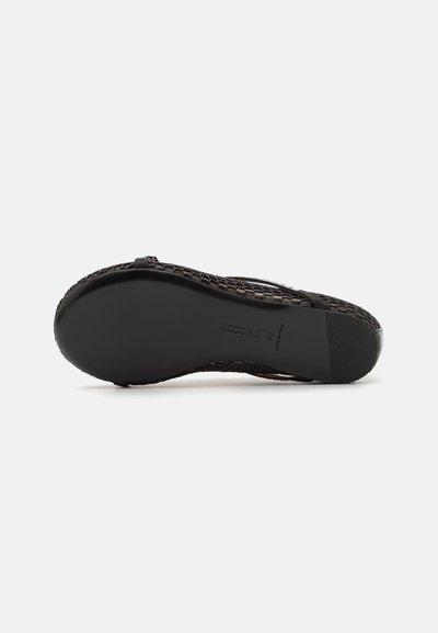Sandalia negra trenzada con suela plana. Presenta un patrón texturizado, punta redonda y un hardware mínimo. Material suave y flexible para mayor comodidad.