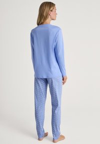 Lichtblauw langemouwen top gecombineerd met lichtblauwe pyjamabroek met een wit hartpatroon. Zachte stof, comfortabele pasvorm en minimalistisch ontwerp.