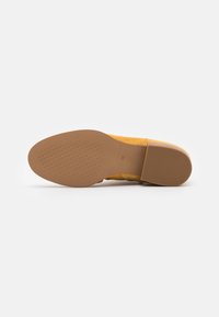 Zapato textil amarillo con parte superior estampada, suela de goma maciza y un pequeño tacón. Talla 38 indicada en la parte inferior.