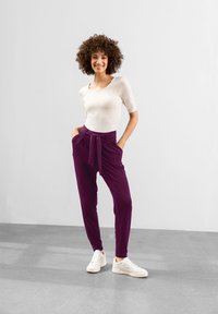 Lila, hög midja byxor med ett knytbälte, med sidofickor, i kombination med en åtsittande krämfärgad topp och vita sneakers. Slät tygstruktur.