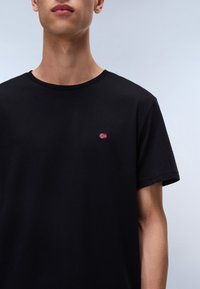 T-shirt en coton noir avec un petit drapeau norvégien brodé sur la poitrine. Encolure ronde et manches courtes. Texture douce.