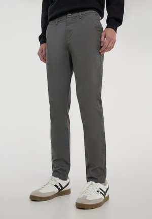 Chino grigi realizzati in tessuto liscio, con una vestibilità slim e tasche classiche. Abbinati a sneakers bianche con accenti grigi e blu navy.