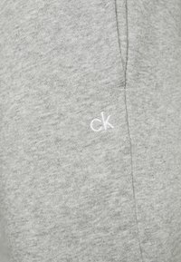 Grau Baumwoll-Sweatpants mit weicher Textur, featuring ein weiß gesticktes "ck" Logo an der Seite und einem nahtlosen Design.