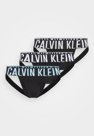 Tři černé pánské boxerky s širokými elastickými pasy, dvě s bílým a jedna se světle modrým nápisem "Calvin Klein".