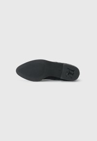 Schwarze Schuhsohle mit strukturiertem Gummioberfläche, die einen glatten Rand und ein eingraviertes Logo aufweist. Das Design beinhaltet dezente Muster für besseren Halt.
