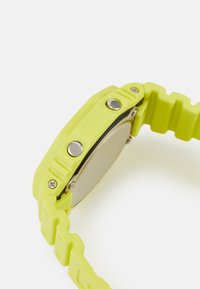 Montre en silicone vert lime avec un bracelet texturé, dotée de boutons argentés et d'un fond métallique. Design de boîtier rectangulaire avec une surface lisse.