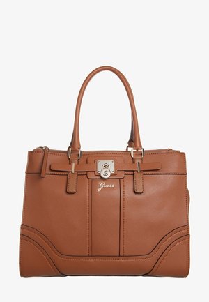 Bruine leren Guess-handtas met dubbele handvatten, voorste sluiting met slot en subtiele stikdetails op een witte achtergrond.