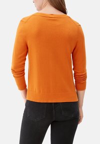 Orange stickad tröja med rund halsringning och ribbade ärmslut och nederkant. Visad från baksidan, tillsammans med svarta jeans. Mjuk textur.