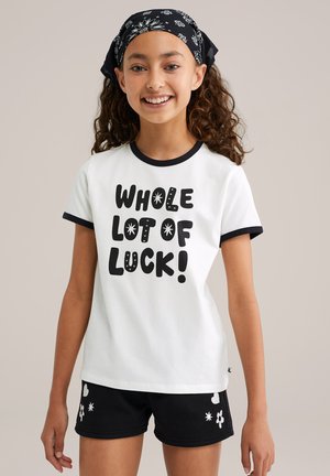 Witte T-shirt met zwarte rand, met opvallende tekst "HELE BOEL GELUK!" in een speelse lettertype. Gecombineerd met zwarte shorts versierd met witte bloemen- en sterontwerpen.