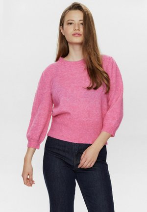 Roze gebreide trui met een ronde hals, zachte textuur en poffende driekwartmouwen, gecombineerd met een donkere spijkerbroek.