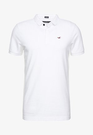 Wit poloshirt met korte mouwen, kraag, twee knopen en een klein rood geborduurd vogellogo op de linkerborst.
