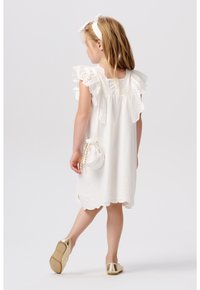 Weißes Baumwollkleid mit Lochstickerei und Rüschenärmeln. Kombiniert mit einer kleinen, runden weißen Tasche und goldenen Ballettschuhen.