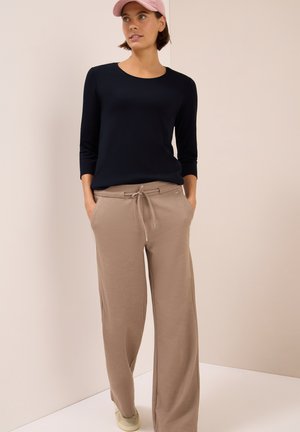 Chemise à manches longues marine associée à un pantalon de jogging large beige clair, avec taille à cordon et poches latérales. Les accessoires incluent une casquette rose.