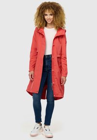 Chaqueta impermeable roja con capucha ajustable, cremallera frontal y dos bolsillos laterales, llevada sobre una camiseta blanca y jeans azules.