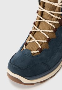 Blauwe suède en bruine gaas wandelschoen met decoratieve stiksels, crèmekleurige veters en een rubberen zool met een contrasterende bruine neus.